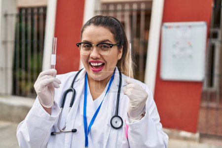 Foto de Joven doctora hispana haciendo prueba nasal de infección por coronavirus celebrando loca y sorprendida por el éxito con los ojos abiertos gritando emocionada. - Imagen libre de derechos