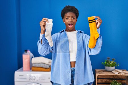 Téléchargez les photos : Femme afro-américaine tenant propres chaussettes sales andy en colère et fou hurlant frustré et furieux, criant de colère. rage et concept agressif. - en image libre de droit
