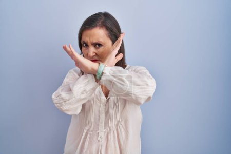 Photo for Middle age hispanic woman standing over blue background rejection expression crossing arms doing negative sign, angry face - Royalty Free Image