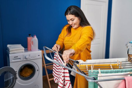 Foto de Young beautiful plus size woman smiling confident hanging clothes on clothesline at laundry room - Imagen libre de derechos