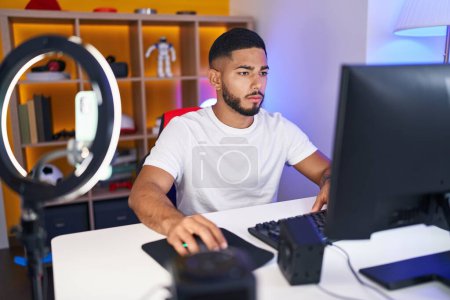 Téléchargez les photos : Jeune homme latin streamer jouer à un jeu vidéo en utilisant l'ordinateur à la salle de jeux - en image libre de droit
