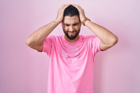 Photo for Hispanic young man standing over pink background suffering from headache desperate and stressed because pain and migraine. hands on head. - Royalty Free Image