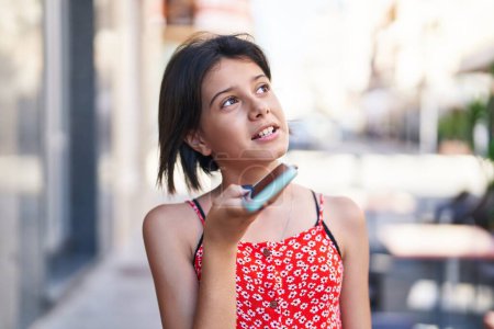 Téléchargez les photos : Adorable fille hispanique parlant sur le smartphone avec une expression sérieuse dans la rue - en image libre de droit