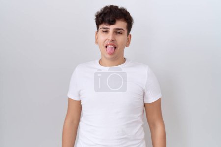 Téléchargez les photos : Jeune homme non binaire portant casual t-shirt blanc collant la langue heureux avec une expression drôle. concept d'émotion. - en image libre de droit