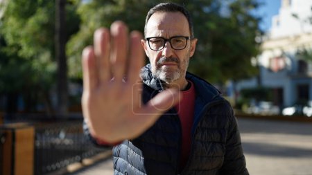 Foto de Middle age man doing stop gesture with hand at park - Imagen libre de derechos