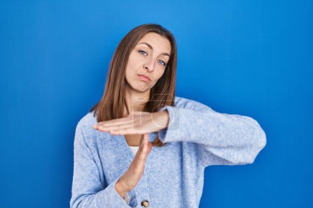 Photo for Young woman standing over blue background doing time out gesture with hands, frustrated and serious face - Royalty Free Image