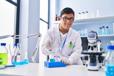 Téléchargez les photos : Homme trisomique portant un uniforme scientifique mesurant le liquide en laboratoire - en image libre de droit