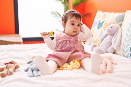 Photo for Adorable hispanic baby playing maraca sitting on bed at bedroom - Royalty Free Image
