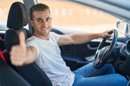 Foto de Joven caucásico hombre conduciendo coche haciendo buen gesto con el pulgar en la calle - Imagen libre de derechos