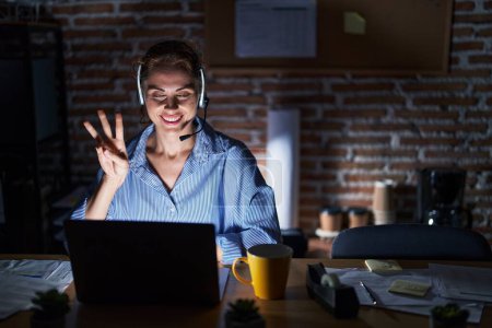 Photo for Beautiful brunette woman working at the office at night showing and pointing up with fingers number three while smiling confident and happy. - Royalty Free Image