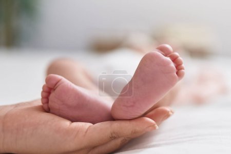 Téléchargez les photos : Adorable bébé hispanique couché sur le lit ayant massage des pieds dans la chambre - en image libre de droit