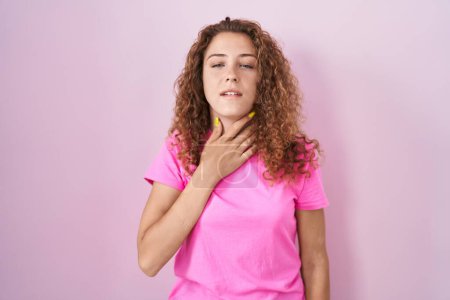Foto de Mujer caucásica joven de pie sobre fondo rosa tocando el cuello doloroso, dolor de garganta para la gripe, la clod y la infección - Imagen libre de derechos