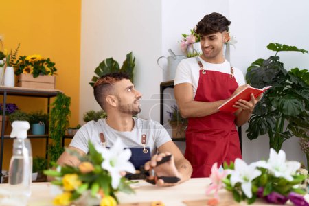 Téléchargez les photos : Two hispanic men florists cutting stem of flower writing on notebook at flower shop - en image libre de droit