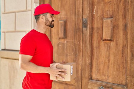 Téléchargez les photos : Jeune homme hispanique courrier tenant paquet à la rue - en image libre de droit