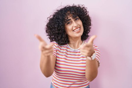 Téléchargez les photos : Young middle east woman standing over pink background pointing fingers to camera with happy and funny face. good energy and vibes. - en image libre de droit