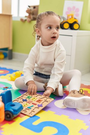 Foto de Adorable chica rubia jugando con matemáticas juego de puzzle sentado en el suelo en el jardín de infantes - Imagen libre de derechos