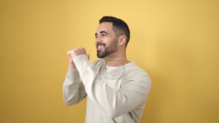 Téléchargez les photos : Jeune homme hispanique souriant danse confiante sur fond jaune isolé - en image libre de droit