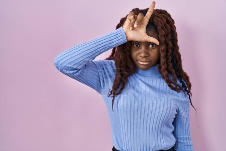 Photo for African woman standing over pink background making fun of people with fingers on forehead doing loser gesture mocking and insulting. - Royalty Free Image