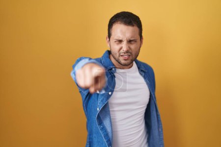 Foto de Hombre hispano de pie sobre fondo amarillo señalando disgustado y frustrado a la cámara, enojado y furioso con usted - Imagen libre de derechos
