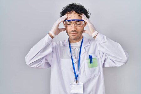 Téléchargez les photos : Homme hispanique travaillant au laboratoire scientifique avec la main sur la tête, maux de tête parce que le stress. migraine souffrant. - en image libre de droit