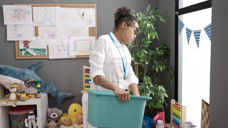 Téléchargez les photos : Africaine américaine enseignante surmenée collectionnant des jouets à la maternelle - en image libre de droit