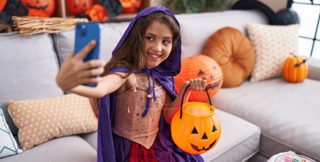 Téléchargez les photos : Adorable fille hispanique portant costume d'Halloween faire selfie par smartphone à la maison - en image libre de droit