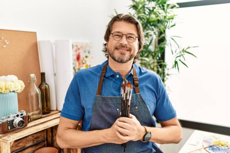 Photo for Middle age caucasian man smiling confident holding paintbrushes at art studio - Royalty Free Image