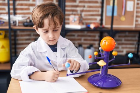 Foto de Adorable hispanic boy astronomer student make planetary work writing on notebook at laboratory classroom - Imagen libre de derechos