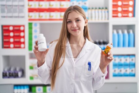 Photo for Young caucasian woman pharmacist smiling confident holding pills bottles at pharmacy - Royalty Free Image