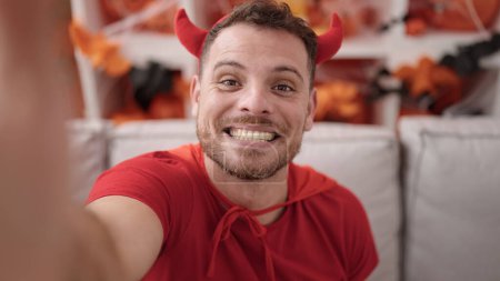 Téléchargez les photos : Jeune homme caucasien portant costume diable prendre selfie photo à la maison - en image libre de droit