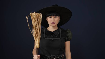 Téléchargez les photos : Young chinese woman wearing witch costume holding broom over isolated black background - en image libre de droit