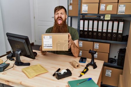 Téléchargez les photos : Rousse homme avec longue barbe travaillant à petite entreprise commerce électronique coller la langue heureux avec drôle d'expression. - en image libre de droit