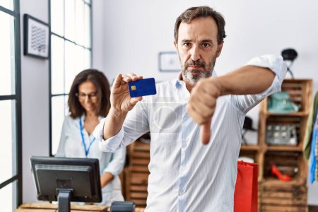 Foto de Hispanic man holding credit card at retail shop with angry face, negative sign showing dislike with thumbs down, rejection concept - Imagen libre de derechos