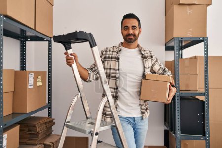 Téléchargez les photos : Jeune homme hispanique ecommerce business worker holding packages standing at office - en image libre de droit