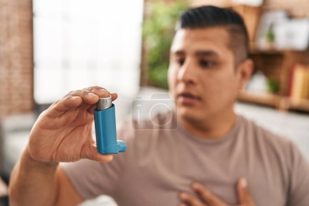 Photo for Young latin man using inhaler sitting on sofa at home - Royalty Free Image