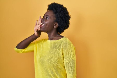 Téléchargez les photos : African young woman standing over yellow studio shouting and screaming loud to side with hand on mouth. communication concept. - en image libre de droit