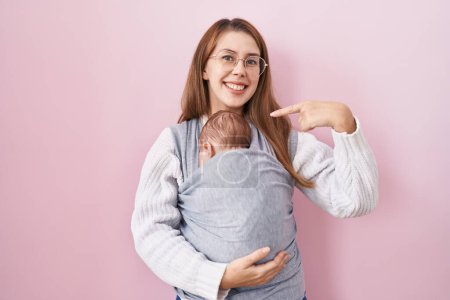 Téléchargez les photos : Jeune femme caucasienne tenant et portant bébé sur un fronde souriant heureux pointant avec la main et le doigt - en image libre de droit