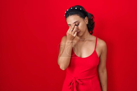 Foto de Mujer hispana joven de pie sobre fondo rojo cansada frotando nariz y ojos sintiendo fatiga y dolor de cabeza. concepto de estrés y frustración. - Imagen libre de derechos