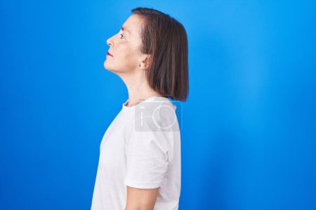 Téléchargez les photos : Moyen Age femme hispanique debout sur fond bleu regardant vers le côté, pose de profil relax avec visage naturel et sourire confiant. - en image libre de droit