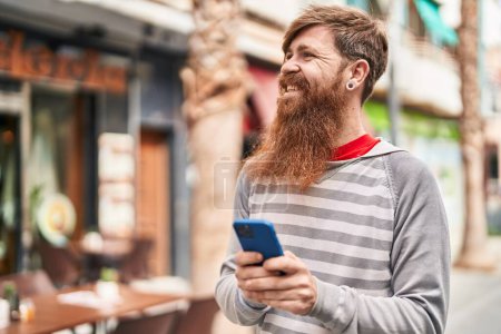 Foto de Young redhead man smiling confident using smartphone at street - Imagen libre de derechos