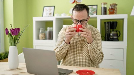 Photo for Middle age man using laptop drinking coffee at home - Royalty Free Image