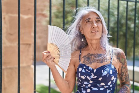 Téléchargez les photos : Middle age grey-haired woman using handfan suffering for hot at street - en image libre de droit