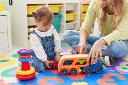 Photo for Teacher and toddler playing with cars toy sitting on floor at kindergarten - Royalty Free Image