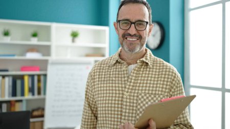 Téléchargez les photos : Middle age man teacher smiling confident holding clipboard at classroom - en image libre de droit