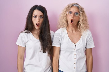 Photo for Mother and daughter standing together over pink background in shock face, looking skeptical and sarcastic, surprised with open mouth - Royalty Free Image