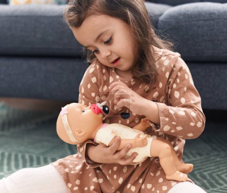 Photo for Adorable hispanic girl hugging baby doll sitting on floor at home - Royalty Free Image