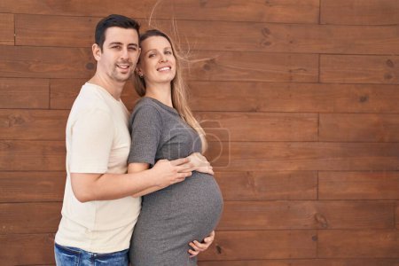 Photo for Man and woman couple hugging each other expecting baby over isolated wooden background - Royalty Free Image