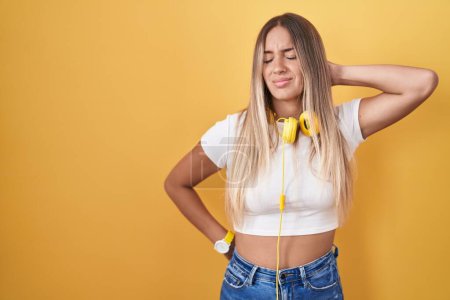 Téléchargez les photos : Young blonde woman standing over yellow background wearing headphones suffering of neck ache injury, touching neck with hand, muscular pain - en image libre de droit