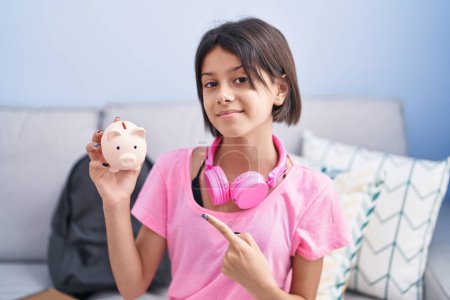 Photo for Young girl holding piggy bank smiling happy pointing with hand and finger - Royalty Free Image