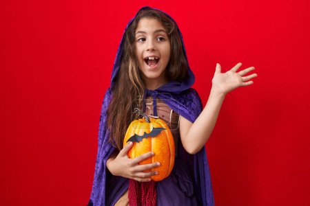 Téléchargez les photos : Petite fille hispanique portant un costume de sorcière d'Halloween célébrant la victoire avec un sourire heureux et l'expression gagnante avec les mains levées - en image libre de droit